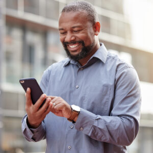Ein Mann hält ein Smartphone in der Hand und lächelt nach unten, während er Teams Phone benutzt.